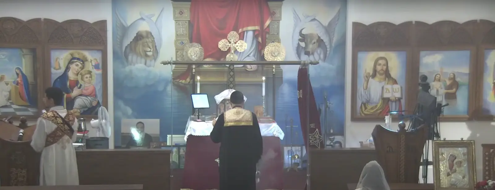 The sanctuary at St. Philopater Mercurius & St. Mina: the iconostasis, its icons of Christ and the Theotokos, and a priest serving at the altar.